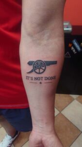 Arsenal ágyú és It’s not done felirat tetoválása az alkaron